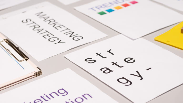 Different pieces of paper are laid out neatly on a table. One reads, "Strategy" and another, "Marketing Strategy"